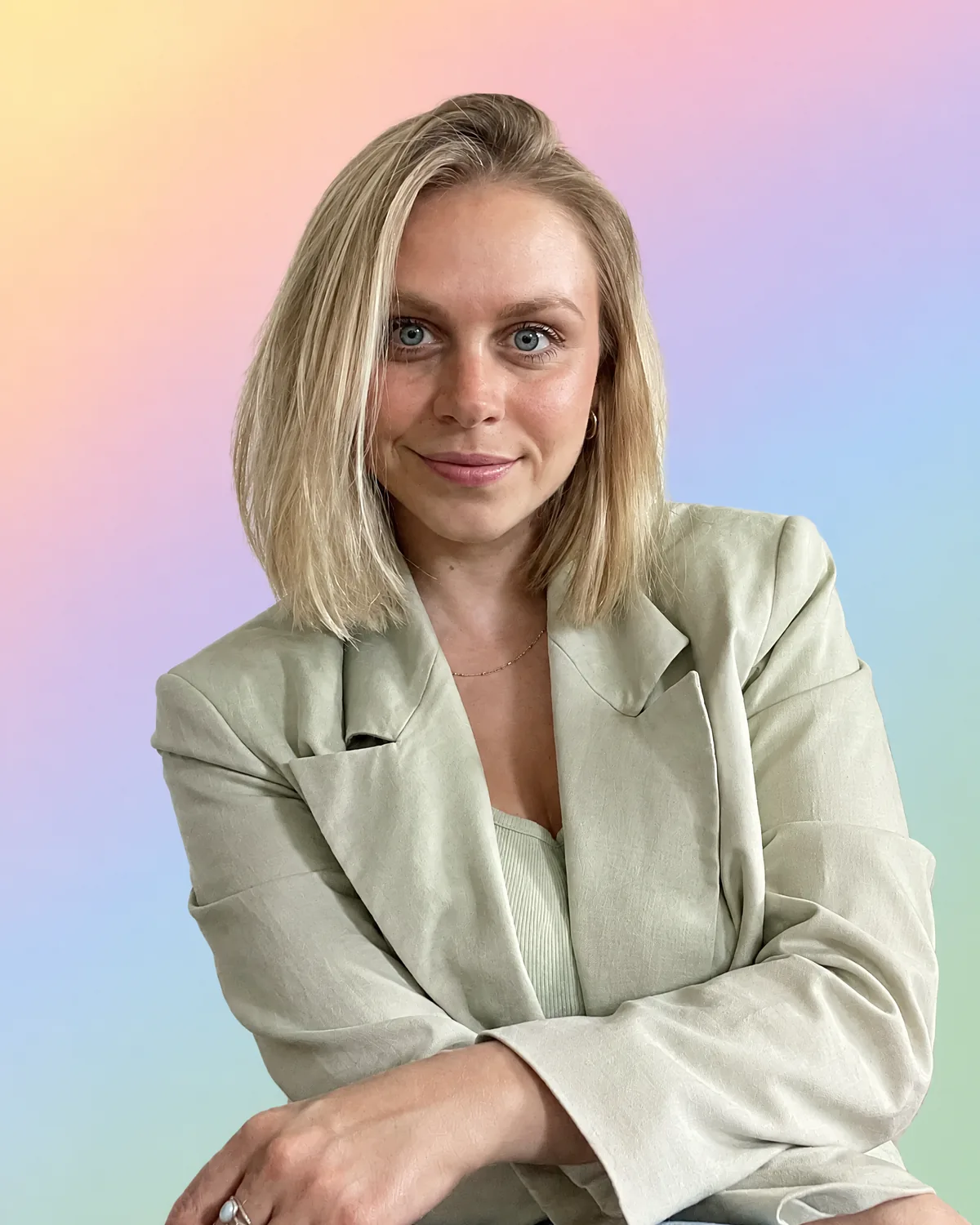 Lisa Routa, color analyst, in a sage linen blazer with her arms crossed, smiling, on a pastel gradient of yellow, peach, pink, lilac, sky blue and sage green