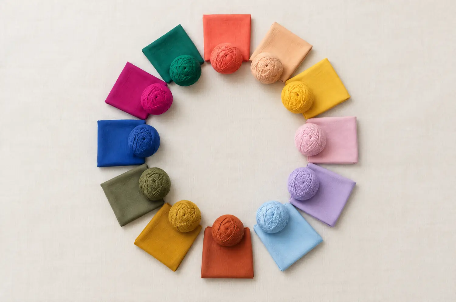 A color wheel of twelve sections made of folded fabrics and balls of wool, one shade per section, around an empty center