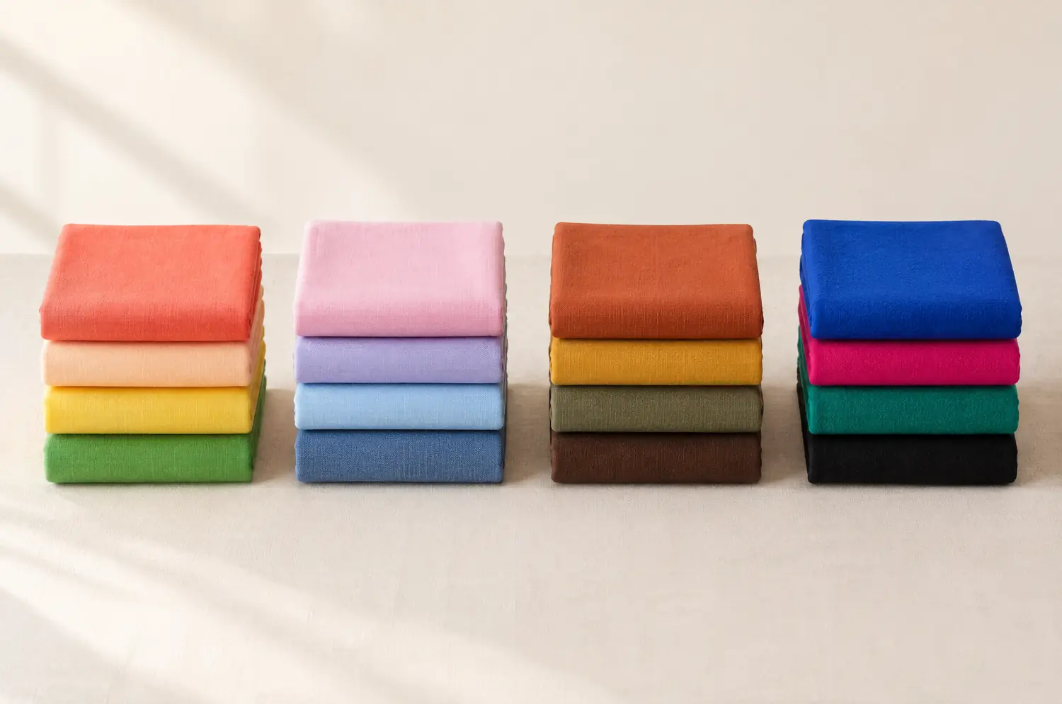 Four stacks of folded fabrics side by side, one per season: Spring, Summer, Autumn and Winter